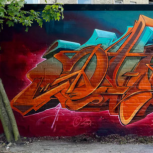 Ein Graffiti in Orange, Beige und Türkis Farben auf einem Stahlblau zu Dunkelrot Verlauf. Gemalt auf einer Wand in Hamburg Barmbek.