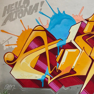 Auf einer Fassade steht Hello Altona, darunter ist eine gelbes Graffiti. Es steht in großen gelben Buchstaben der Name Ohm One. Im Hintergrund sind bunte Farb Splashes zu sehen.