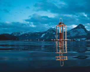 Advent am Wolfgangsee mit schwimmender Laterne vor der verschneiten Winterlandschaft