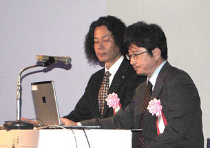 尖閣諸島開拓の日の式典で講演する日本野鳥の会の安藤会員室長(左)と山本チーフ=14日午後、市民会館中ホール
