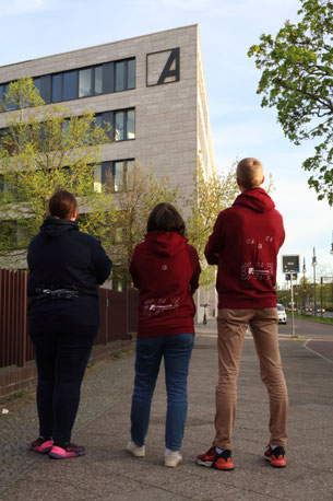 3 Personen tragen Pullover des neuen Merch vor dem Gebäude der Konrad-Adenauer-Stiftung.