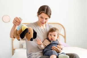 Mutter mit Baby auf dem Schoß und der Musikspieluhr Little Mateys Hund von LÄSSIG