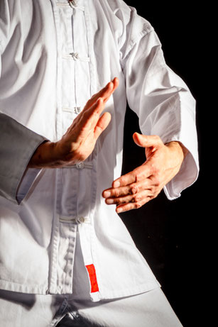 Eine Person trainiert Tai Chi in weißer chinesischer Kleidung. Man sieht seine Körpermitte und seine beiden Hände.