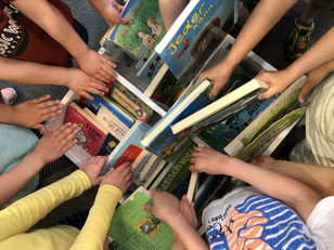 Foto von vielen Kinderhänden die in eine Kiste voller Bücher greifen