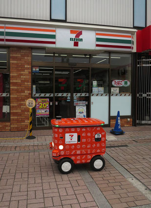南大沢のバス停付近を無人の台車がトコトコ動いていた。人が近づくと停車する。これは「セブンイレブン」が南大沢の２店舗で実証実験している自動搬送ロボット。飲食店内での配膳ロボットは体験しているが、店外への配送…上手く行くことを願っている。私は頼まないけどね。2025.6.8　【写真⑥：八王子市南大沢1-29】