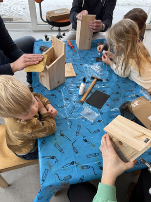 Eltrn und Kinder sitzen an einem Tisch und bauen Nistkästen für Vögel