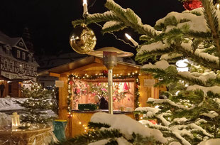 Szene auf Berleburger Weihnachtsmarkt mit verschneitem Weihnachtsbaum und Bude im Hintergrund.