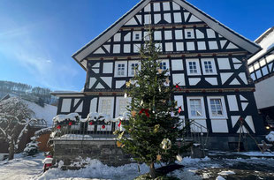 Großer Weihnachtsbaum steht vor einem Fachwerkhaus in der verschneiten Ortschaft Diedenshausen.