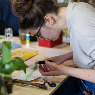 Vrouw kijkt geconcentreerd naar creatie van een stempel op een tafel.