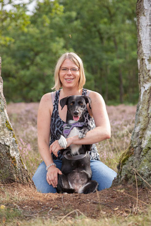 Hundetrainerin Rebecca mit ihrem eigenen Hund auf einer Wiese neben einem Baum