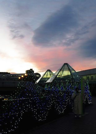 駅前のスーパーマーケットを出ると駅舎の上に茜雲(あかねぐも)。年末のイルミネーションが却って侘しさを感じさせる。