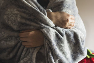 Person hält mit den Händen eine wärmende Decke um sich