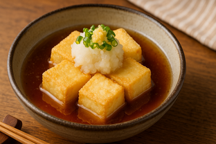 Silky agedashi tofu cubes in hot dashi broth topped with grated daikon, ginger, and green onions, ceramic Japanese bowl.