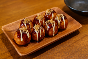 Takoyaki octopus balls topped with sauce, mayonnaise, and bonito flakes, served on a wooden plate at an izakaya table.