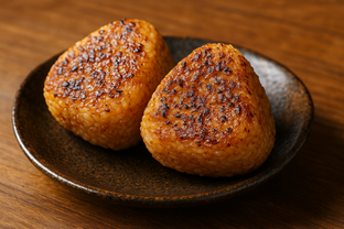 Grilled yaki onigiri rice balls brushed with soy sauce, slightly charred surface, served on a small Japanese ceramic plate.