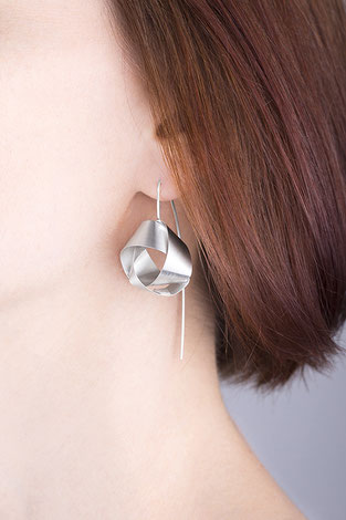 Ein raffiniert mit sich selbst verschlungenes Silberband bildet das zentrale Element der Ohrhänger NOLA. Ihre klare Eleganz und das seidig matt und geheimnisvoll schimmernde Silber machen NOLA unwiderstehlich. Die Ohrhänger sind wunderbar schwerelos