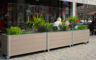 Gastronomie-Windschutz Casablanca Blumen: Beige Pflanzmodule auf Rollen mit integriertem Glasschutz zur Abgrenzung eines Straßencafés auf Kopfsteinpflaster