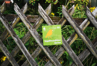 Die Plakette Vogelfreundlicher Garten ziert einen Gartenzaun.