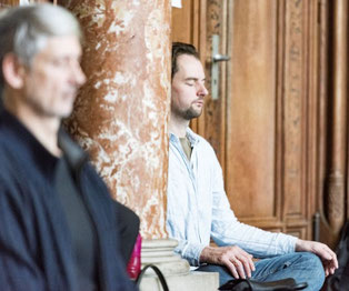 Zwei Männer sitzen in einem Raum und meditieren. 