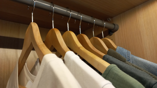 Kleiderbügel aus Holz hängen mit weißen, grünen und blauen Oberteilen an einer Kleiderstange im Schrank