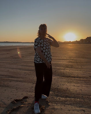 Eine Frau macht Taiji am Strand bei Sonnenaufgang.