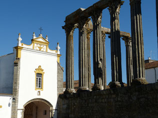 Säulen-Reste des römischen Diana-Tempels in Évora mit Kirche im Hintergrund vor blauem Himmel