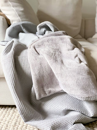 Sofadecke aus Waffelpique in grau mit muschelweichem Fleece in Silbergrau. Die Decke liegt auf einem Sofa