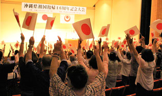 閉会前には、入り口で手渡された「日の丸」の旗を掲げ、聴衆が万歳三唱した=13日、豊見城市中央公民館