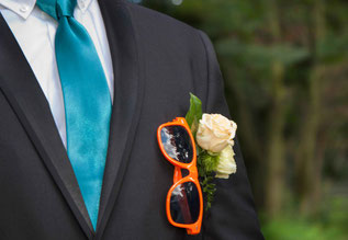 Farbaufnahme Bräutigam, orange Brille, Blume im Anzug steckend, starker Ausschnitt, Außenaufnahme