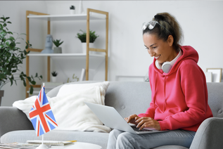 Frau am Tisch mit Laptop und englischer Fahne.