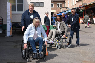 Amazon-Mitarbeiter begleiten Personen, die Rollstühle ausprobieren beim Fahren