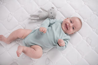 Fröhliches Baby liegend auf Matratze von Träumeland