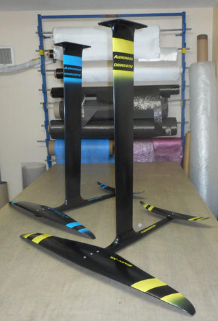 2 foils Aeromod pour wingfoil, un noir et jaune, l'autre noir et bleu, assemblés, dans l'atelier