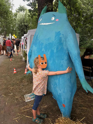 Ein Kind umarmt eine große blaube Pappmachée-Figur, Kit Klimamonster