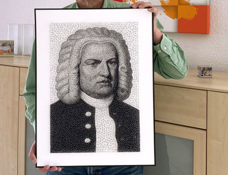 Eine Person mit grünem Hemd, deren Kopf man nicht sieht präsentiert ein Fadenbild mit Rahmen in einem Wohnumfeld. Das Fadenbild zeigt das Porträt von Bach in Schwarzweiß. Um Bach herum ist ein weißes Passepartout.