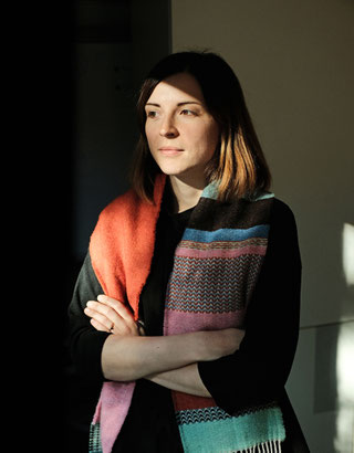 Dorothee Elmiger hat schulterlange Haare und trägt einen bunten Schal. Sie hat die Arme um den Körper geschlungen.