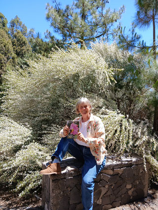 mujer-con-libro-en-las-manos-sentada-en-un-muro-delante-arbustos-con-flores-blancas-la-palma