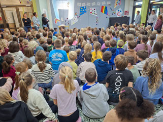 Kinder sitzen versammelt im Foyer und singen gemeinsam