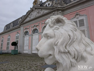 Steinerner Löwe vor einem rosafarbenen Barockgebäude.