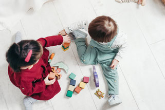 2 Kinder spielen auf dem Boden mit Bauklötzen aus Holz