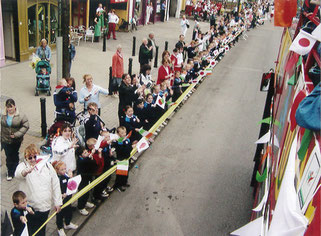 日本選手団のバス（右側）に歓迎の旗を振るニューブリッジの人々