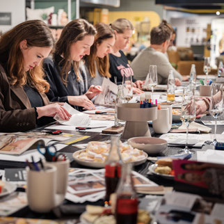 viele Frauen sitzen an großem Tisch und basteln an Collagen 