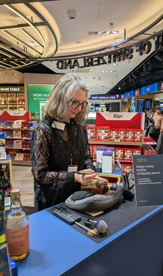 Sigrid Bengel konzentriert bei der Live-Glasgravur einer Whiskyflasche am Whisky Collective Stand im Flughafen Zürich, Mai 2026