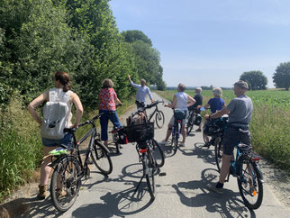 Eine Gruppe Radfahrer auf einem Feldweg hört einem Referenten zu
