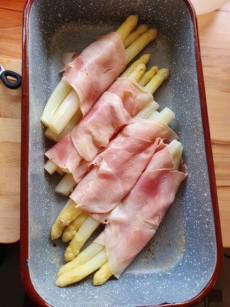 Weißer Stangenspargel in Schinken eingewickelt in einer Auflaufform