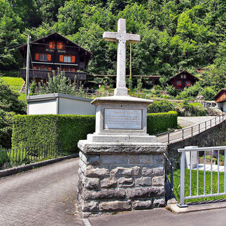 La croix de Tell avec le poème sur la mort de Tell, de Ludwig Uhland (1787-1862) à Bürglen. En arrière-plan, la maison de Tell.