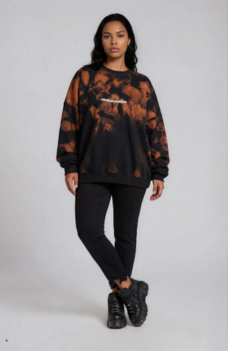 model wearing an oversized black and orange washed unisex sweater with black boots and black distressed pants 
