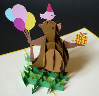Carte pop-up anniversaire enfant avec un ours offrant un cadeau et des ballons