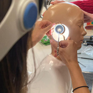 Henkel forceps being used on a manikin head by someone wearing loupes with a headlight 