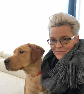 Autismus Coach Dagmar Eiken mit Therapiehund Casper. Auf dem Bild sieht man Dagmar Eiken, eine Frau mittleren Alters. Sie hat kurzen, wasserstoffblonden Haaren. Sie trägt einen dunklen Schal und eine Brille, während sie freundlich in die Kamera lächelt. A